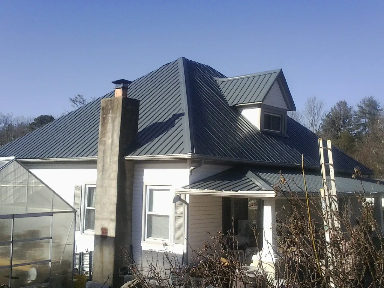 Dark blue standing seam metal roof on a white farmhouse with dormer — Slate & Tile Roof Repair by Roofing Brothers in Leslie