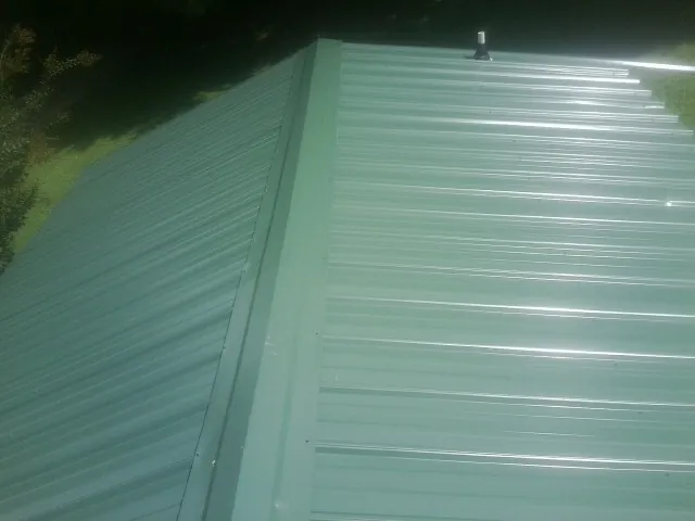 New green metal panels meeting at the ridge of a roof — Flat Roof Repair work by our crew in Leslie
