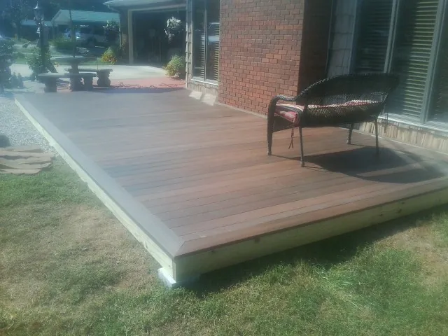 New wood deck and wicker chair beside a brick house in Leslie
