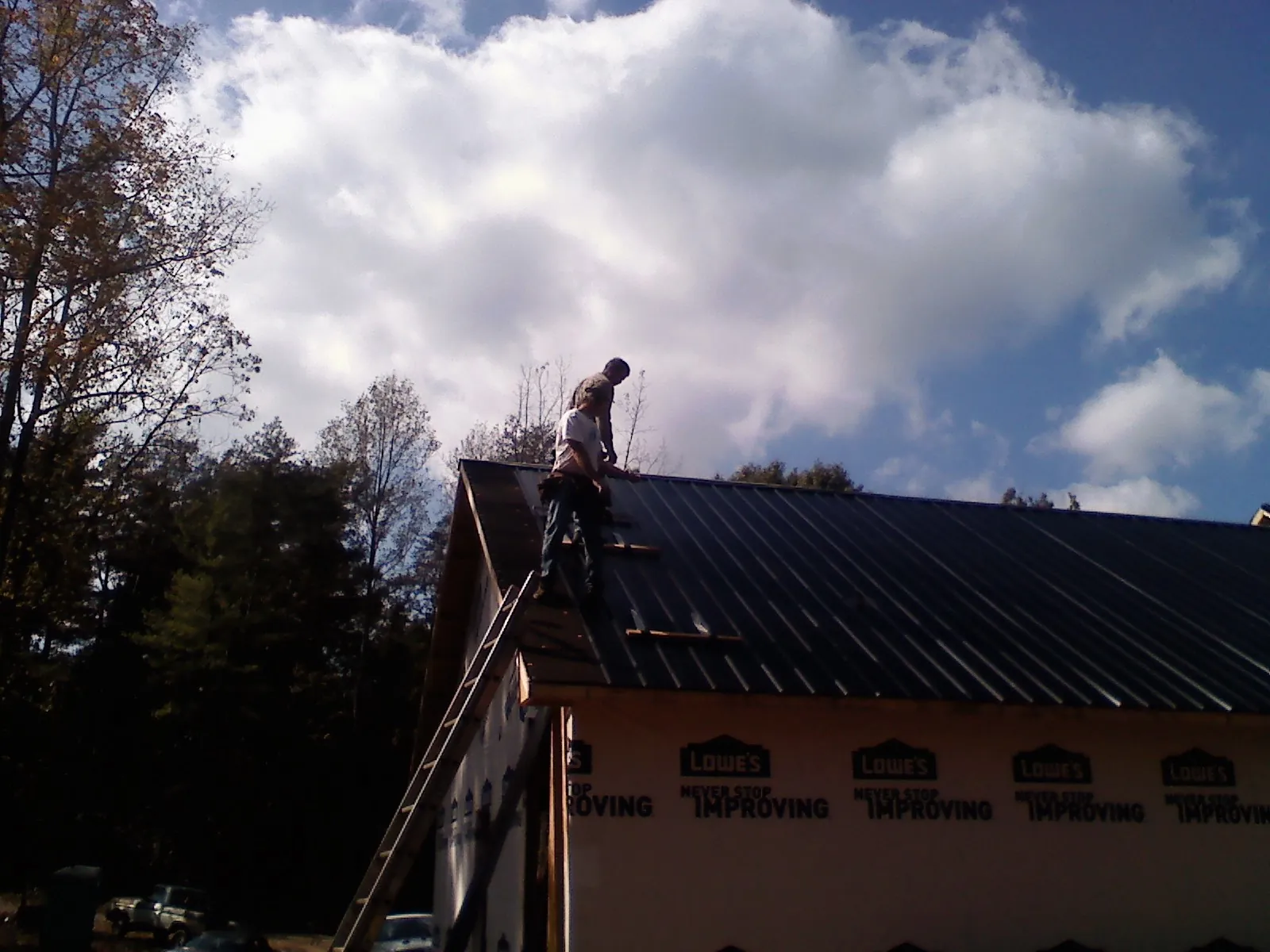 Roofer fastening dark metal panels high against a cloudy sky, from a Roof Inspection job in Leslie